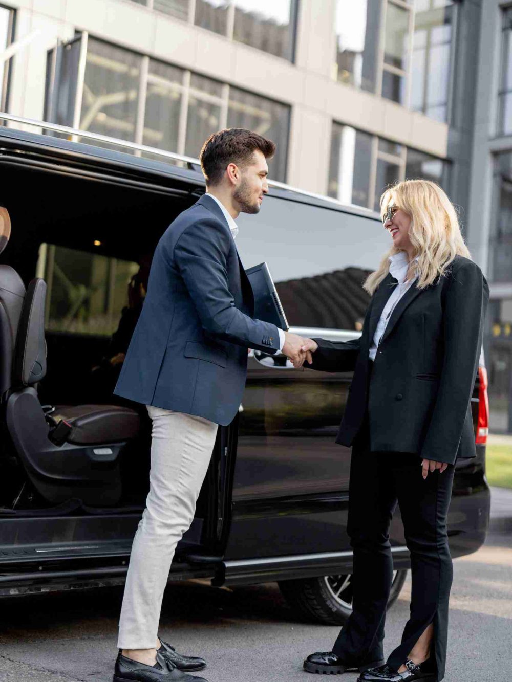 Female chauffeur greets the businessman while helping him to get out of the minivan taxi. Concept of personal driver, luxury taxi for business people